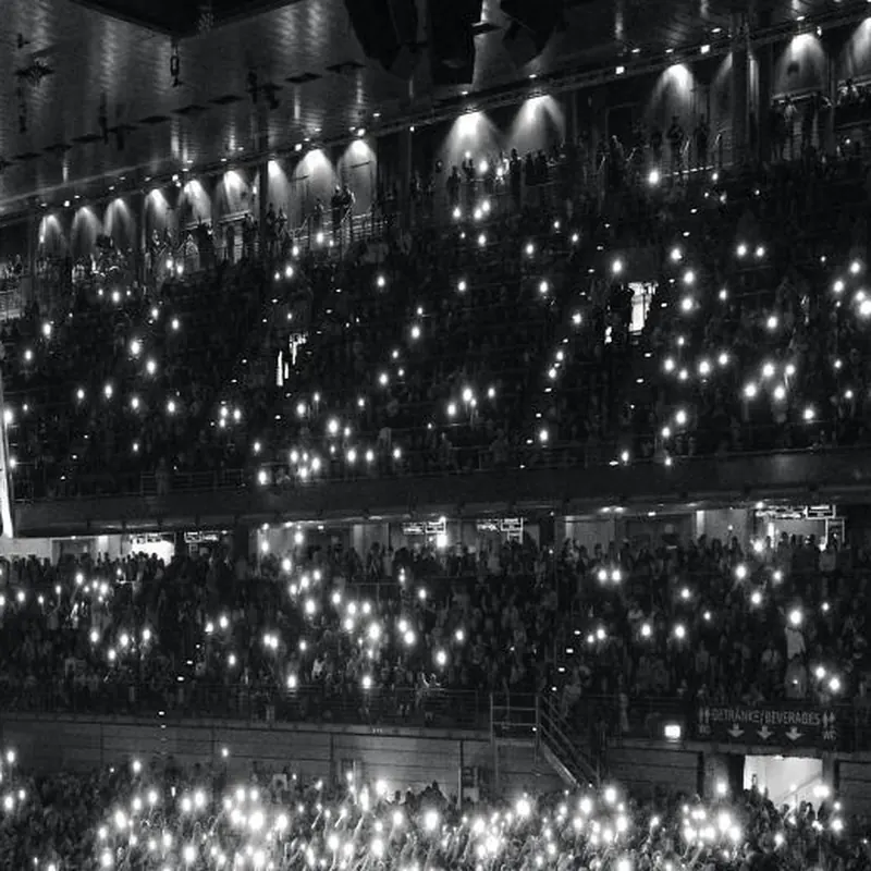 Recinto multitudinario con luces de celulares en las gradas